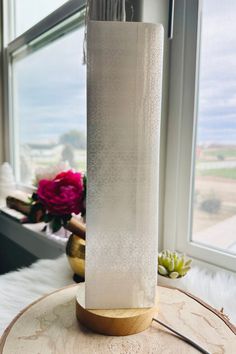 a tall white vase sitting on top of a wooden table next to a large window