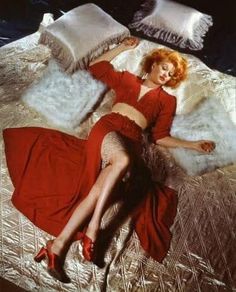 a woman laying on top of a bed in a red dress and high heels with her legs crossed