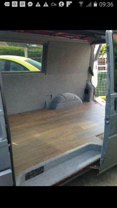 the interior of a van with wood flooring and doors opened to reveal a bed