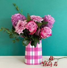 a pink and white checkered vase filled with purple flowers