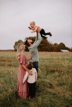 a man and woman holding a baby up in the air while they stand in a field