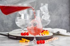 a pitcher pouring red wine into two glasses with candy canes and candies on the side