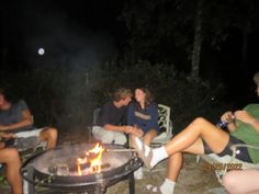 four people sitting around a fire pit at night