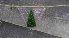 a green christmas tree ornament hanging from a string on a wooden fence with water droplets