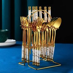 gold and white utensils are stacked up in a holder on a blue tablecloth