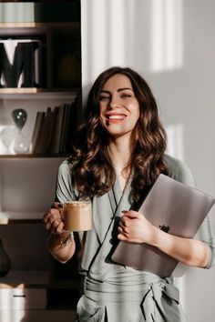 a woman holding a laptop and coffee in her hand