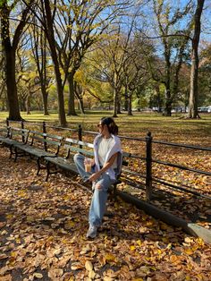 a person sitting on a bench in a park with leaves all over the ground and trees