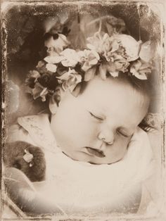 an old photo of a baby with flowers on her head and eyes closed, sleeping