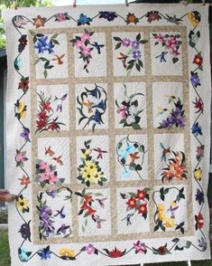 a woman holding up a quilt with flowers on it