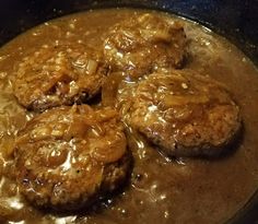 hamburger patties are being cooked in a skillet with gravy on top