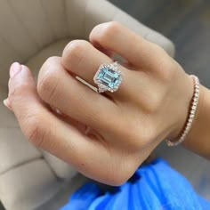 a woman's hand wearing a ring with an aqua topazte surrounded by diamonds