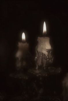 three lit candles sitting on top of a table in front of a black background,