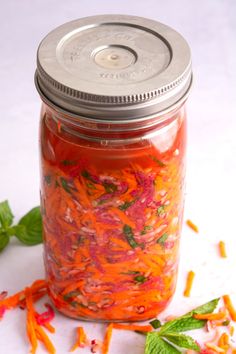 a jar filled with red and orange flowers on top of a white table next to leaves