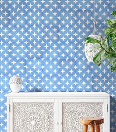 a white cabinet sitting next to a plant on top of a wooden table in front of a blue wall