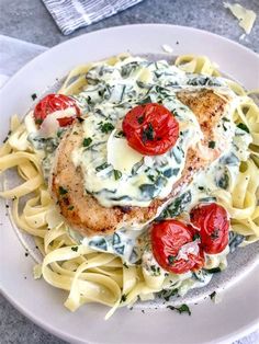 a white plate topped with pasta and chicken covered in sauce, tomatoes and spinach