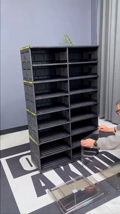 a man sitting on the floor in front of a book shelf filled with black books