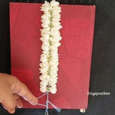 a hand is holding a string attached to a book with white flowers on the cover