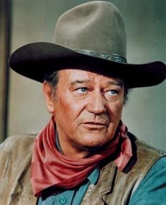 a man in a cowboy hat and vest smiles at the camera with his hand on his hip