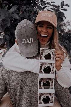 a woman holding onto a man's hat while he holds up his dad's photo