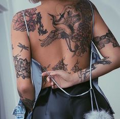 a woman with tattoos on her back holding a black bag and looking at the camera