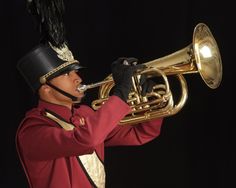 a man in a red uniform playing a brass trumpet with a black hat on his head