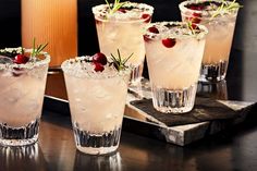 four glasses filled with ice and cherries on top of a wooden table next to a bottle