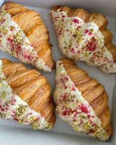 four croissants in a box with white frosting and sprinkles