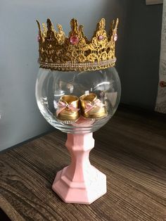 there is a glass bowl with gold shoes in it and a crown on the top