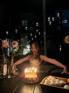 a woman standing in front of a birthday cake with lit candles on top of it