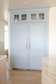 a large white cabinet with glass doors in the middle of a wooden floored room