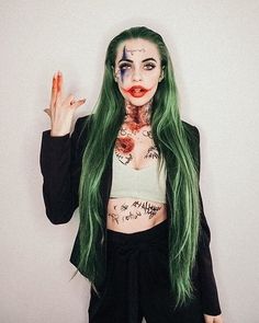 a woman with green hair and makeup holding her hand up to the side while wearing black pants