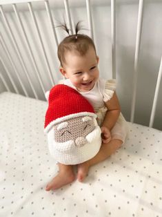 a baby sitting in a crib with a santa hat on it's head