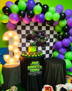 a monster truck themed birthday party with neon balloons and cake on the table, checkerboard backdrop