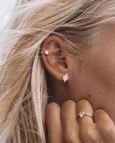 a woman with blonde hair is wearing two star shaped ear cuffs and has her hand under her ear