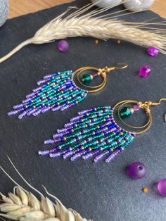 two pairs of beaded earrings sitting on top of a black surface next to purple beads