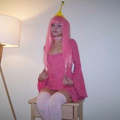 a woman with pink hair sitting on top of a wooden chair next to a lamp