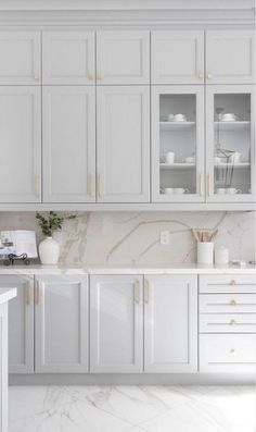 a kitchen with white cabinets and marble counter tops, gold trim on the door handles