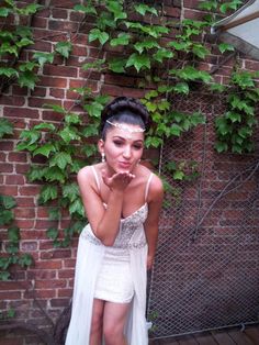 a woman in a white dress standing next to a brick wall with ivy growing on it