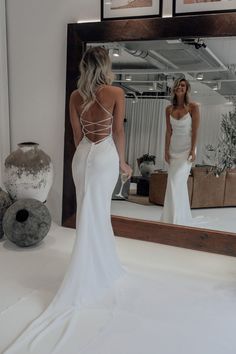 a woman standing in front of a mirror wearing a white wedding dress with open back