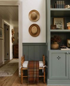 two hats are hanging on the wall next to a chair and bookshelf in a hallway