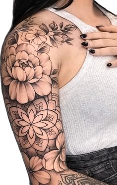 a woman with black and white tattoos on her arm, wearing a tank top that has flowers on it