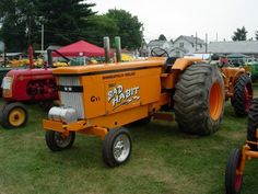 an orange tractor sitting on top of a lush green field next to other farm equipment