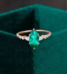 an emerald colored ring with two diamonds on it in a green velvet box, close up