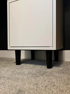 a white cabinet sitting on top of a carpeted floor next to a black wall