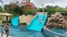 several people are playing in the pool while others watch from the water slide and swim