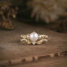 a pearl and diamond ring sitting on top of a wooden table next to a feather