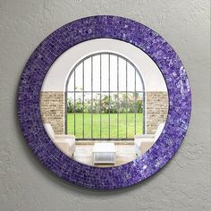 a round mirror with purple glass in front of a brick wall and white couches