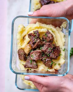 a person holding a glass container filled with meat and potatoes