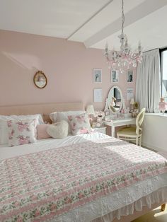 a bedroom with pink walls, white bedding and a chandelier hanging from the ceiling