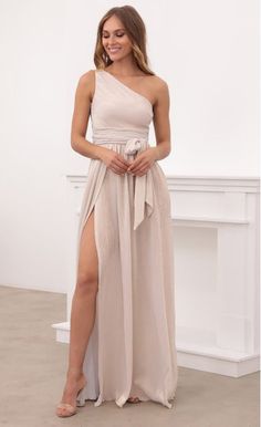 a woman wearing a beige one shoulder dress with thigh high slits and an asymmetrical belt